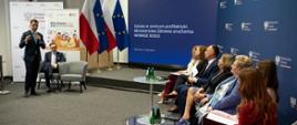 Przedstawiciele Ministerstwa Edukacji Narodowej i Ministerstwa Zdrowia siedzą w rzędzie. W tle za nimi wyświetlana jest prezentacja z tytułem: Szkoła w centrum profilaktyki. Ministerstwo Zdrowia uruchamia WOBASZ DZIECI.