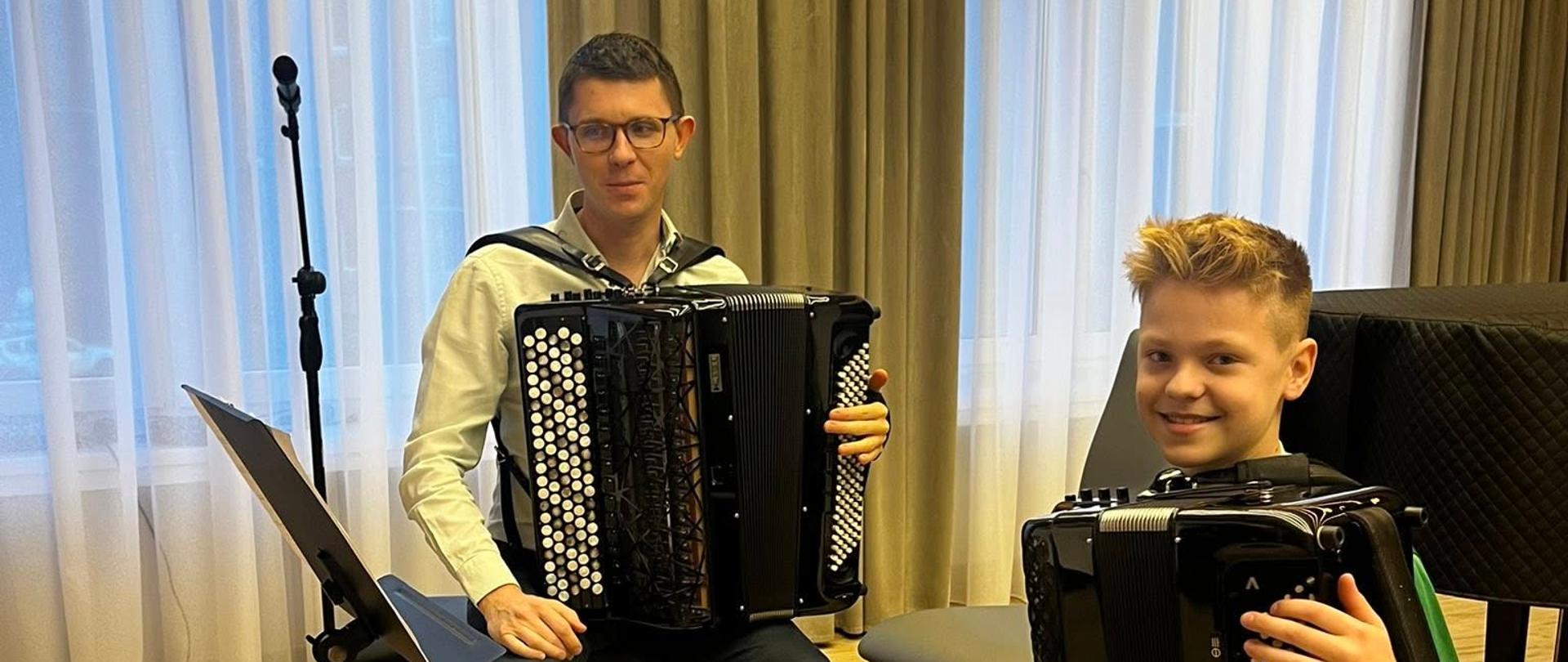 Uczeń podczas lekcji akordeonu, z lewej strony nauczyciel, przed nimi pulpit.