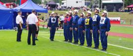 Widok z boku. Drużyna OSP Przytkowice podczas konkurencji musztry. Dowódca pododdziału w trakcie wydawania komendy.