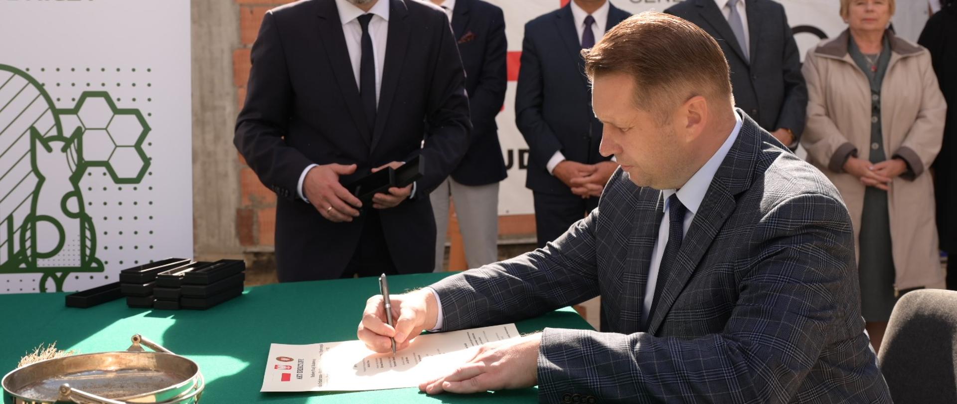 Przemysław Czarnek siedzi przy stole i podpisuje akt Uniwersytecie Przyrodniczym w Lublinie. 