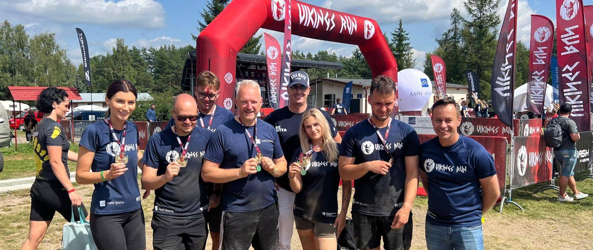 Osiem osób stoi w sportowych strojach z medalami na szyi 