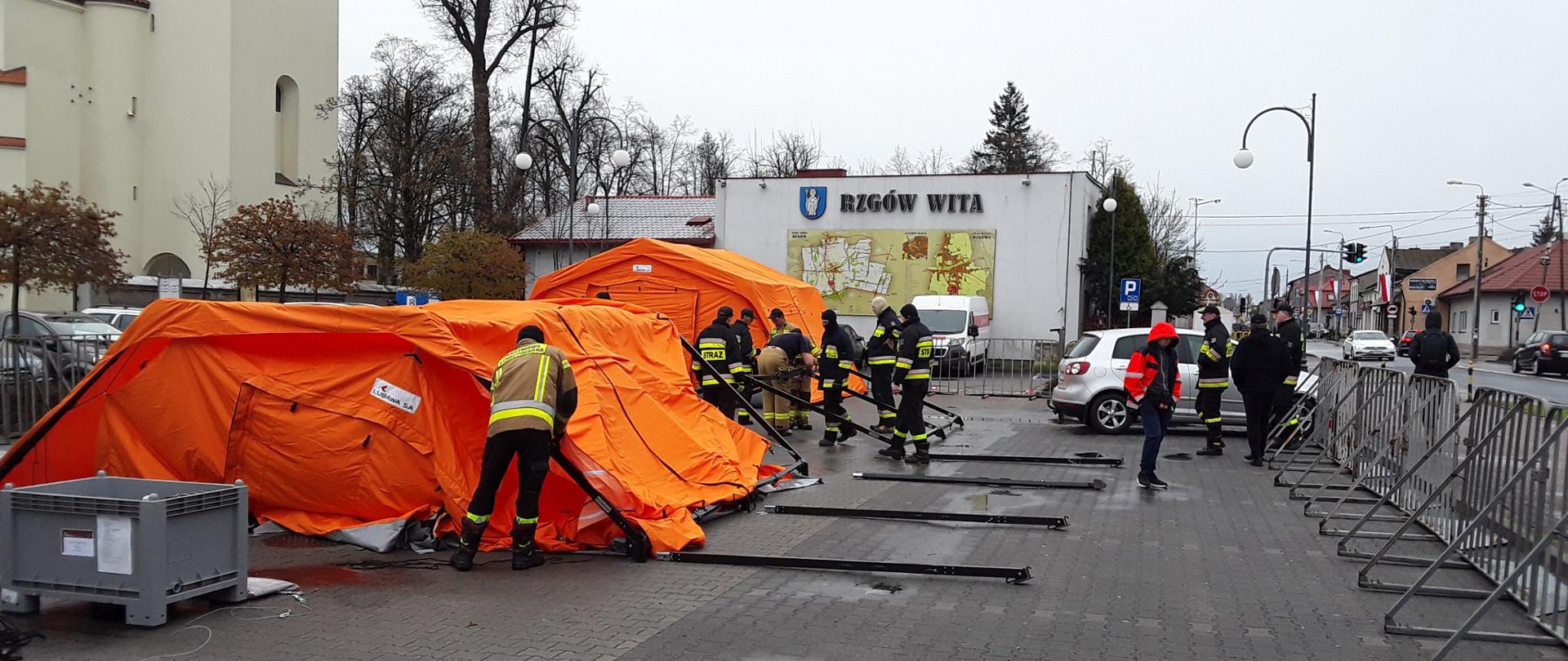 Zdjęcie przedstawia strażaków rozstawiających namioty pneumatyczne w miejscu mobilnego punktu szczepień w Rzgowie ul. Łódzka