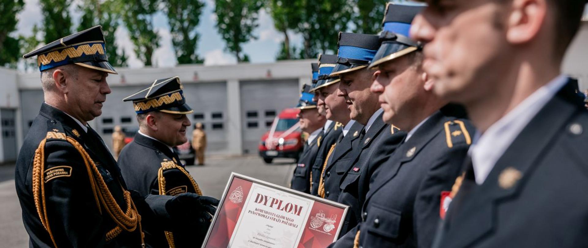 Nadbryg. Arkadiusz Przybyła i nadbryg. Krzysztof Kędryk wręczają Dyplomy Komendanta Głównego PSP. Strażacy w mundurach galowych.