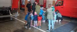 
Zdjęcie przedstawia grupę dzieci podczas zapoznania ze sprzętem strażackim w pomieszczeniu garażu na tle pojazdów strażackich koloru czerwonego.