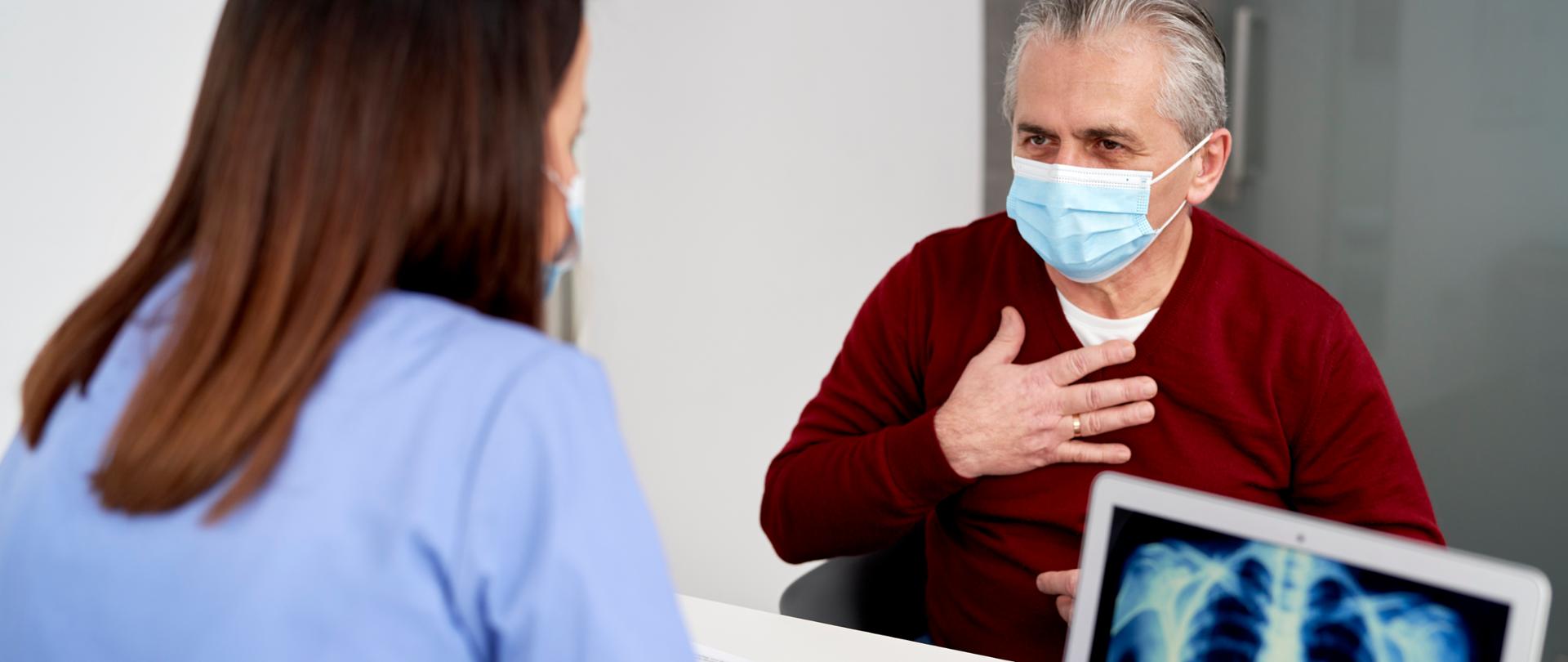 mężczyzna siedzi przed lekarką i trzyma się za piersi 