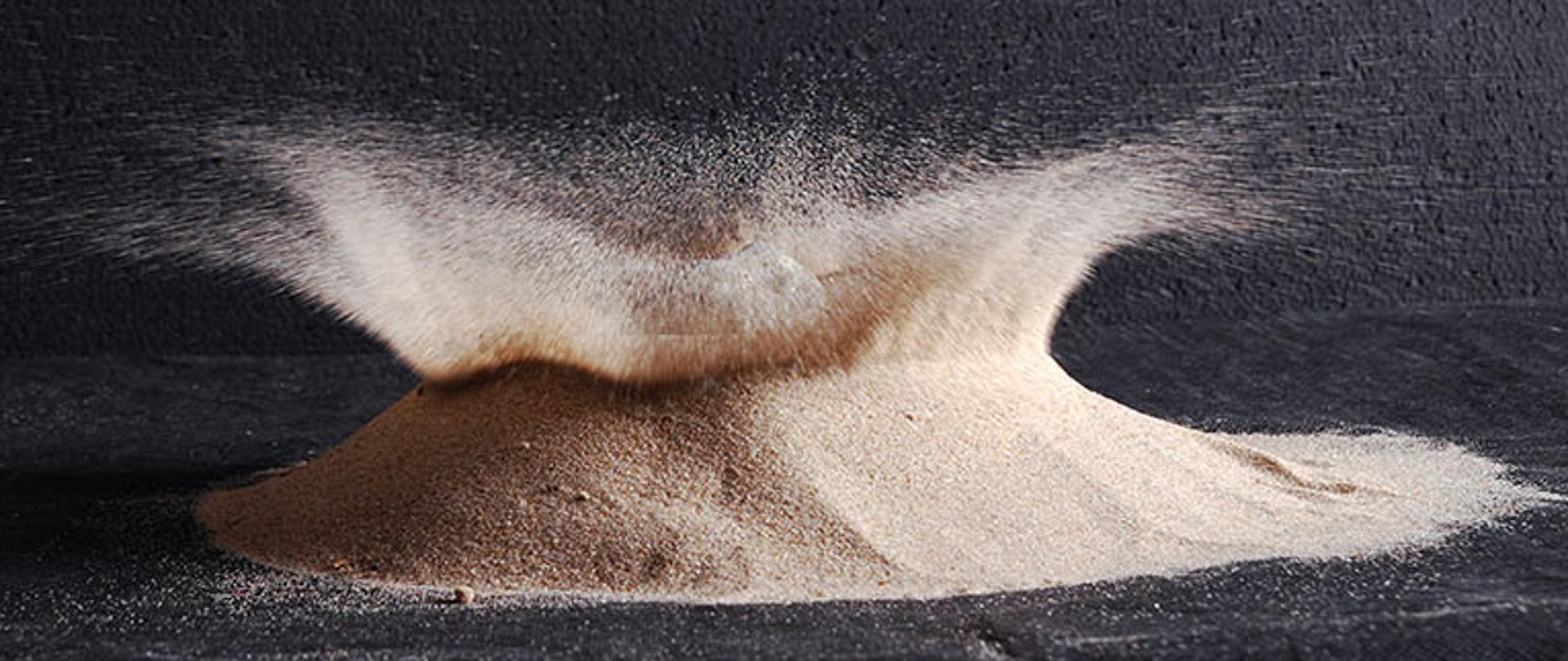 Zdjęcie ilustruje rozprysk niewielkiej ilości piasku w wyniku upadku kamienia.