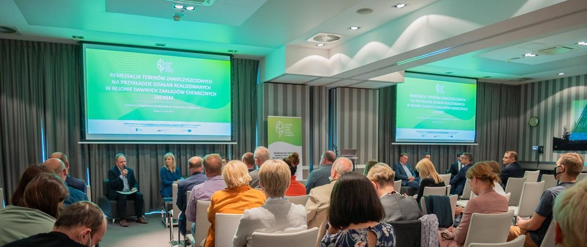 D. Choromański z mikrofonem siedzi na scenie, przed nim widownia