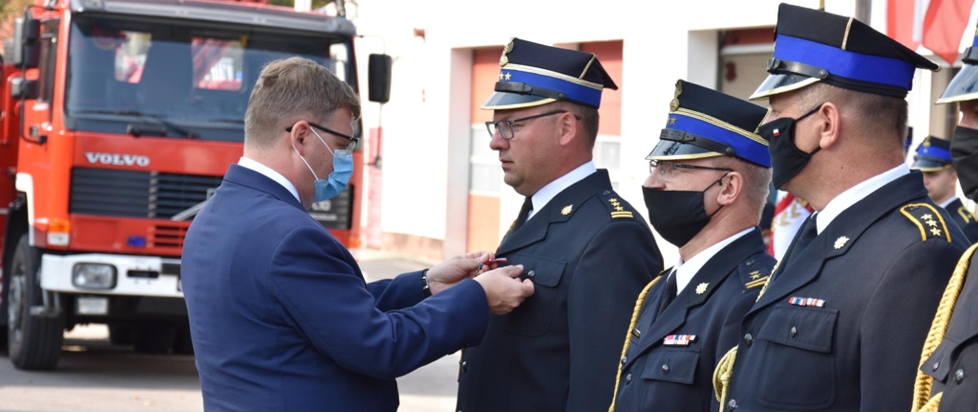 Artur Chojecki Wojewoda Warmińsko-Mazurski wręczający Złotą Odznaką Zasłużony dla Ochrony Przeciwpożarowej dla st. bryg. Tomasza Ostrowskiego