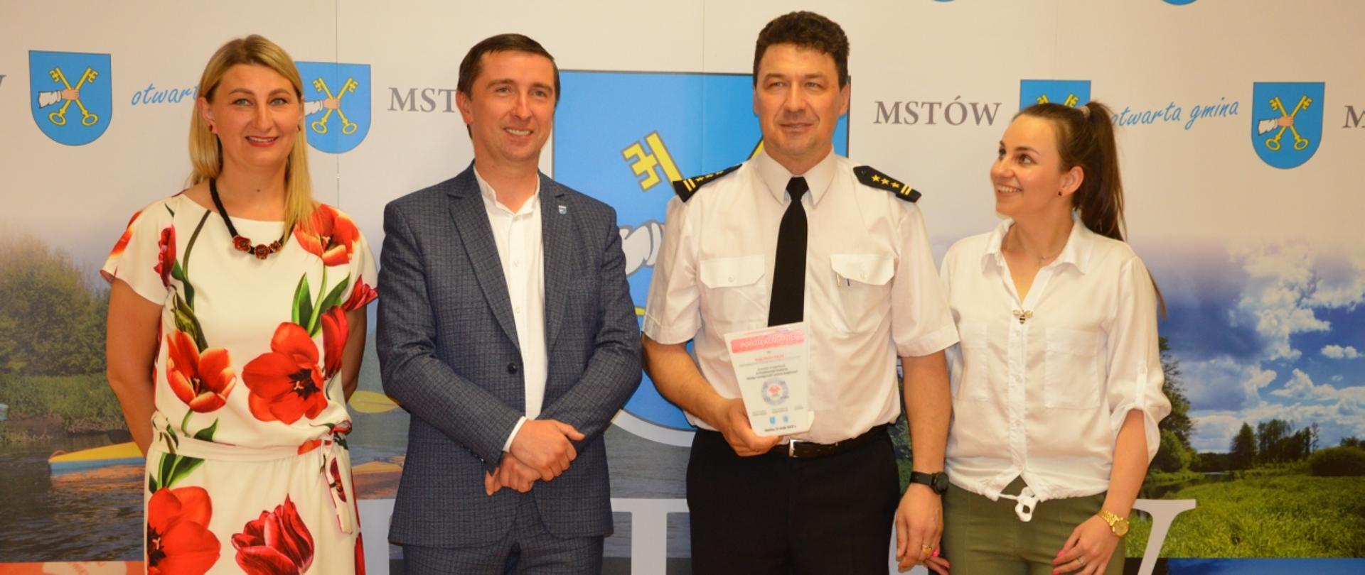 Na zdjęciu Komendant Centralnej Szkoły PSP, dwie kobiety oraz mężczyzna pozujący na tle baneru reklamowego