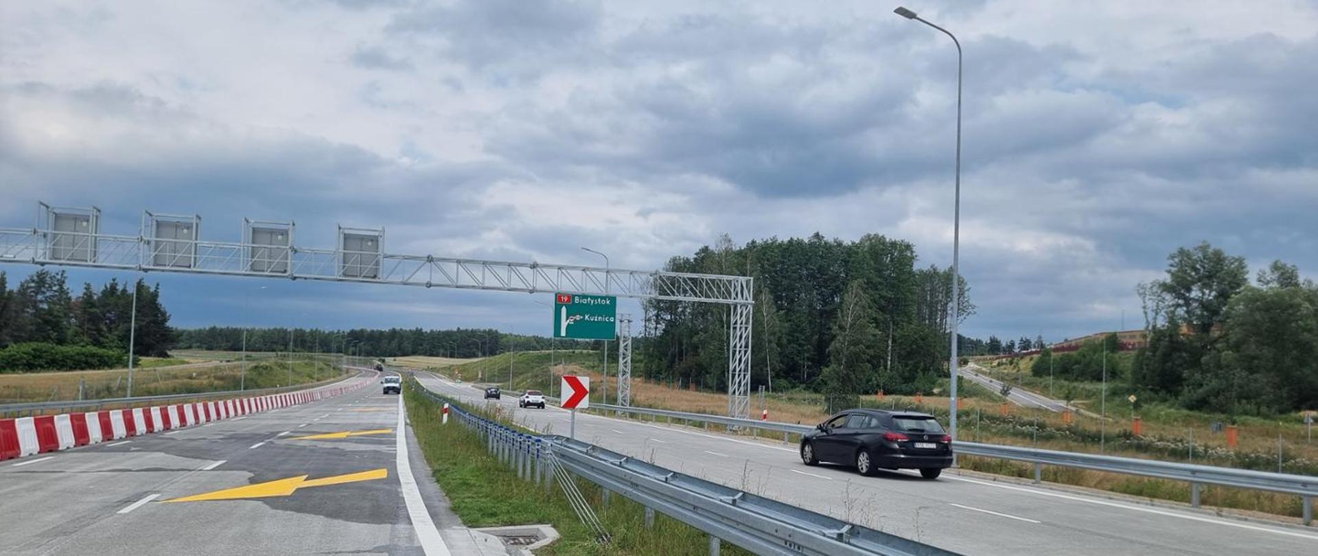 Dwie jezdnie, w środku pas rozdziału z barierą, na prawej jezdni trzy auta jedno za drugim