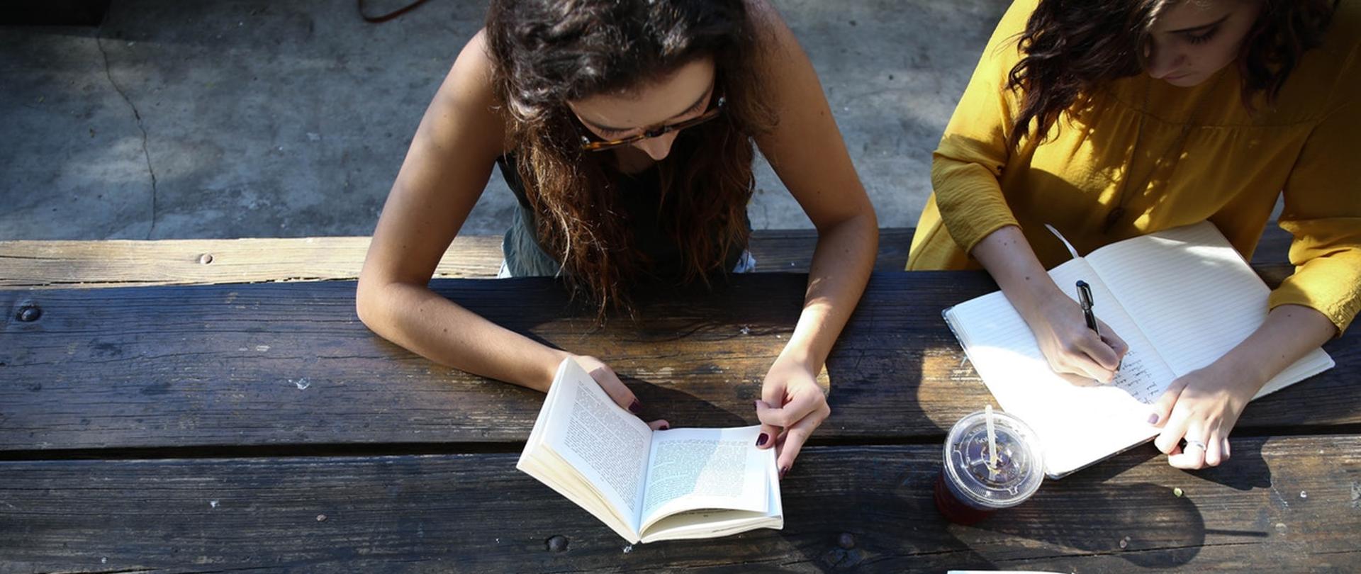 Na zdjęciu studenci czytają książki na drewnianym stole.