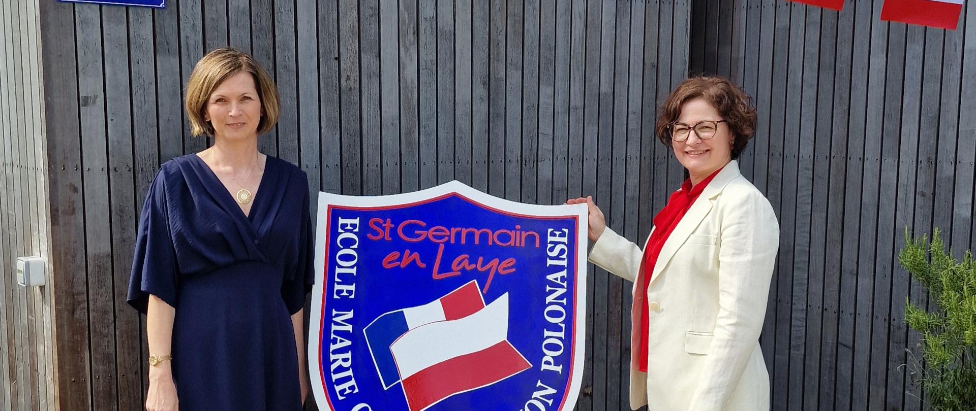 Tarcza Szkoły Podstawowej Marie Curie w Saint-Germain-en-Laye. Po obu jej stronach stoją dwie kobiety.