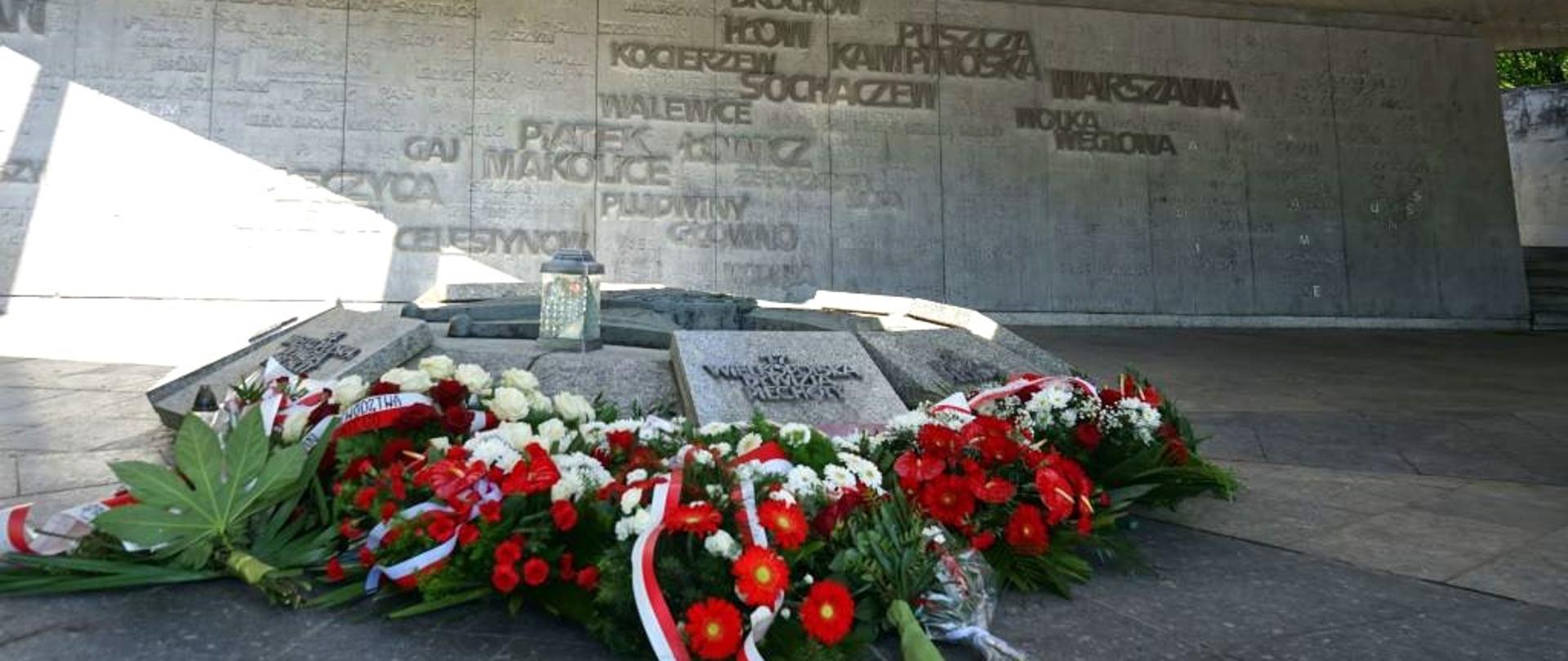 biało czerwone wiązanki kwiatów leżą pod pomnikiem