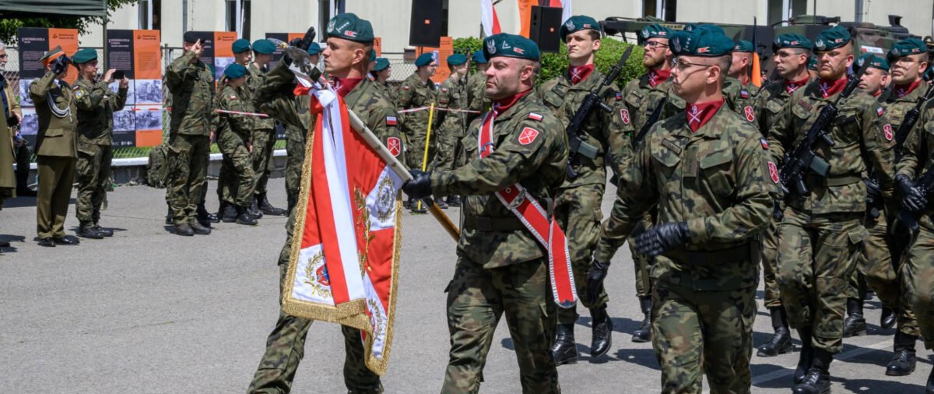 Zdjęcie przedstawia żołnierzy idących ze sztandarem