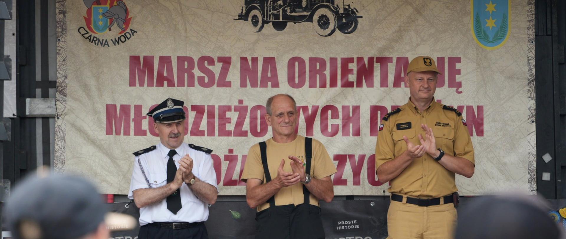 Zdjęcie przedstawia przedstawicieli współorganizatorów marszu na tle baneru reklamowego. 