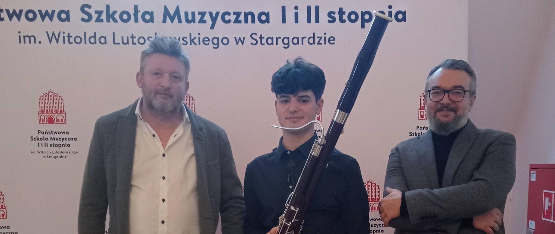 Nauczyciele razem z uczniem stoją na tle ścianki