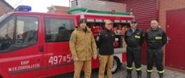 Na zdjęciu znajduje się samochód pożarniczy oraz czworo strażaków w mundurach