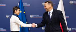 Minister Radosław Sikorski z unijną Komisarz ds. Rozszerzenia Martą Kos na tle flag Unii Europejskiej i Polski
