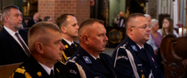 Funkcjonariusze służb mundurowych oraz zaproszeni goście siedzą w ławce w kościele obok siebie.
