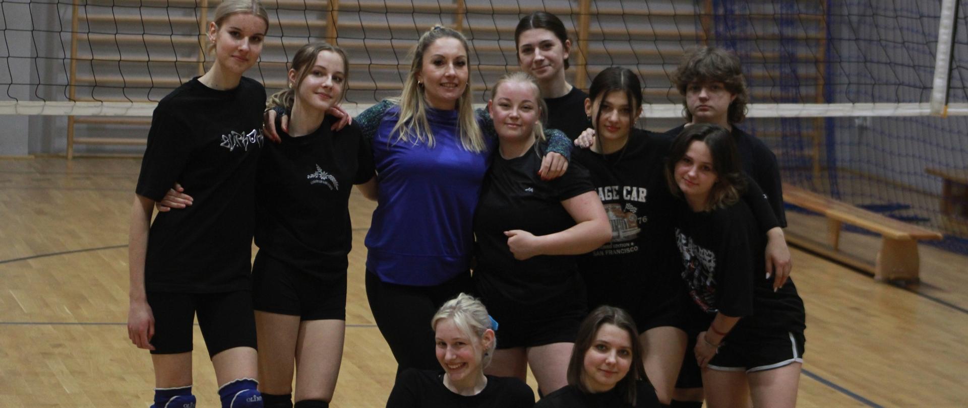 Grupa dziewięciu dziewcząt wraz z trenerką pozuje do zdjęcia.