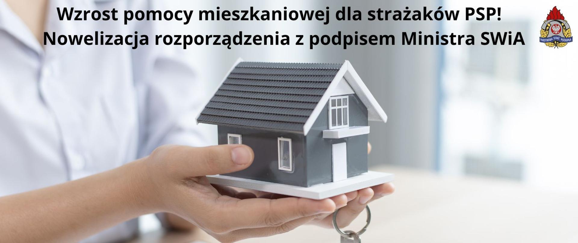 Na dłoniach ludzkich stoi mały szary domek, nad obrazkiem napis" Wzrost pomocy mieszkaniowej dla strażaków PSP – nowelizacja rozporządzenia z podpisem Ministra Spraw Wewnętrznych i Administracji"