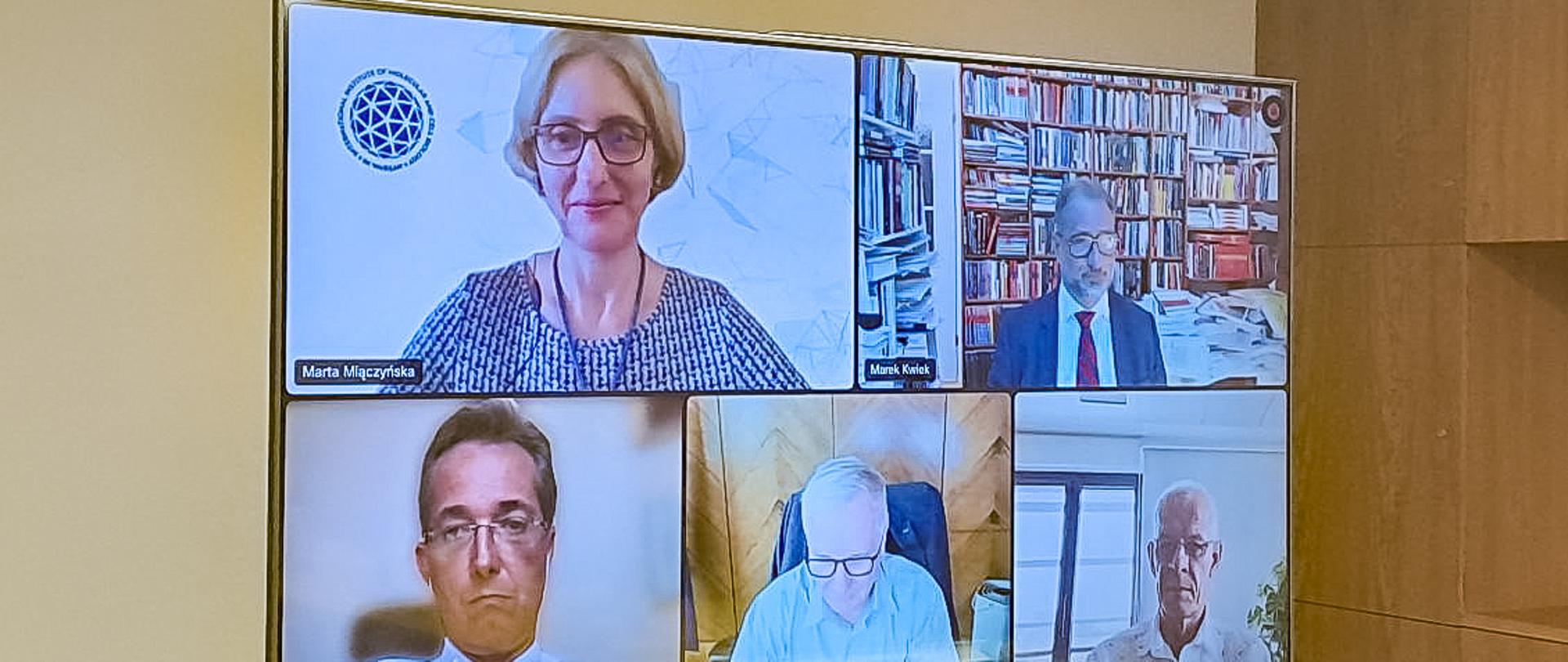 Widok na duży monitor, na którym widać twarze kilku uczestników posiedzenia on-line.