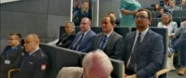 Wiceminister Włodzimierz Bernacki siedzi w czasie otwarcia konferencji wraz z innymi uczestnikami na auli. 