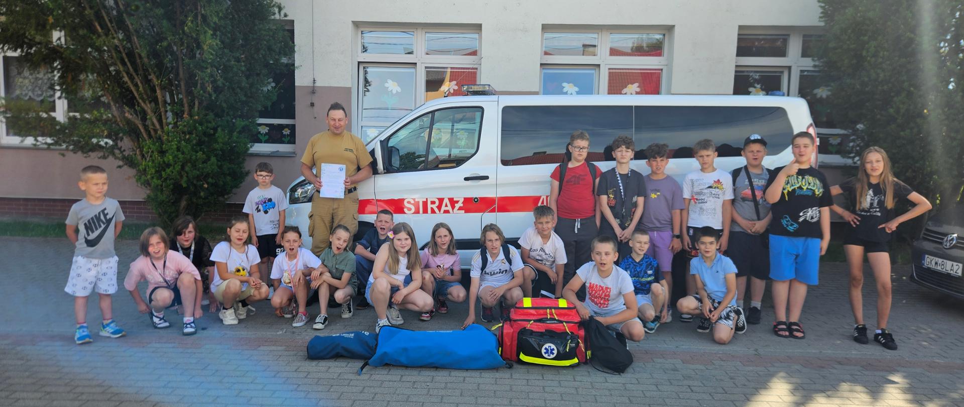 Uczniowie stoją przed szkołą przy samochodzie