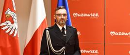Dh Mariusz Skomorucha z OSP Kosów Lacki Strażakiem Miesiąca na Mazowszu 15.07.2024 - na zdjęciu wyróżniony z nagrodą, w tle flaga polski i szyld mazowsza