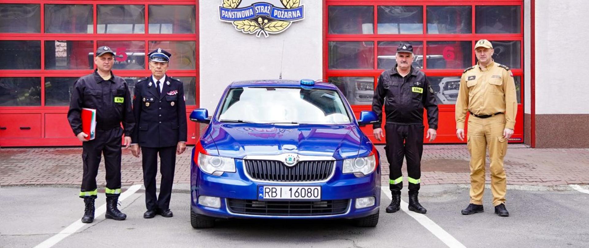 Zdjęcie przedstawia komendanta powiatowego z Ustrzyk Dolnych, dwóch druhów z OSP Brelików oraz prezesa zarządu oddziału powiatowego ZOSP RP. Stoją Oni przed garażami JRG Ustrzyki Dolne przy samochodzie Skoda Superb. 