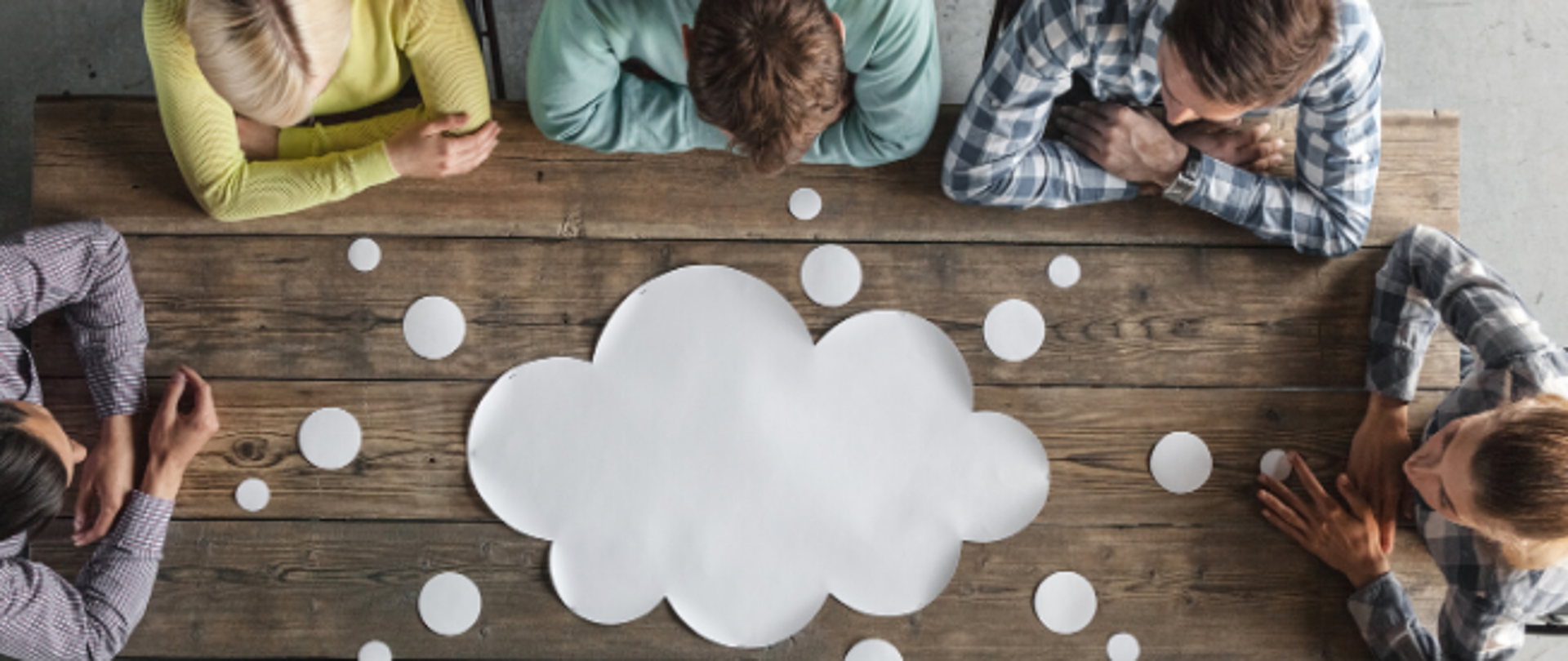 Pięć osób, od lewej: mężczyzna w koszulę w kratkę i ciemnych włosach, kobieta, blondynka w żółtej bluzce, mężczyzna w jasnozielonym sweterku, mężczyzna w koszuli w kratkę i kobieta w koszuli w kratkę z kucykiem, siedzi przy drewnianym stole, na którym leży papierowa chmurka