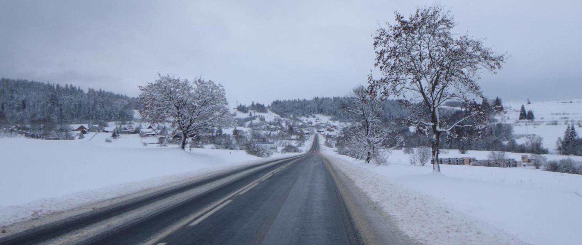Droga w zaśnieżonym terenie, w tle pagórki, las