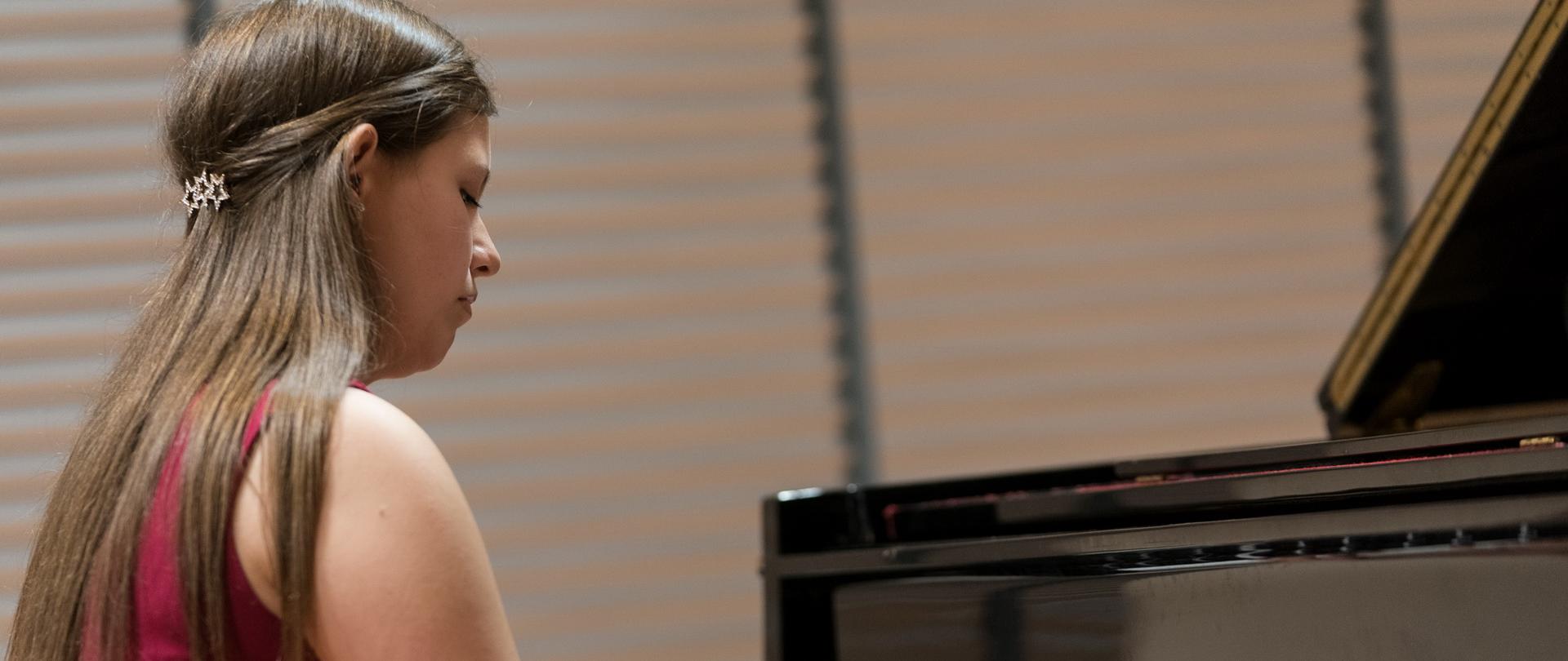 Gabriela Lityńska siedzi przy fortepianie ubrana w czerwoną sukienkę, ręce na klawiaturze.