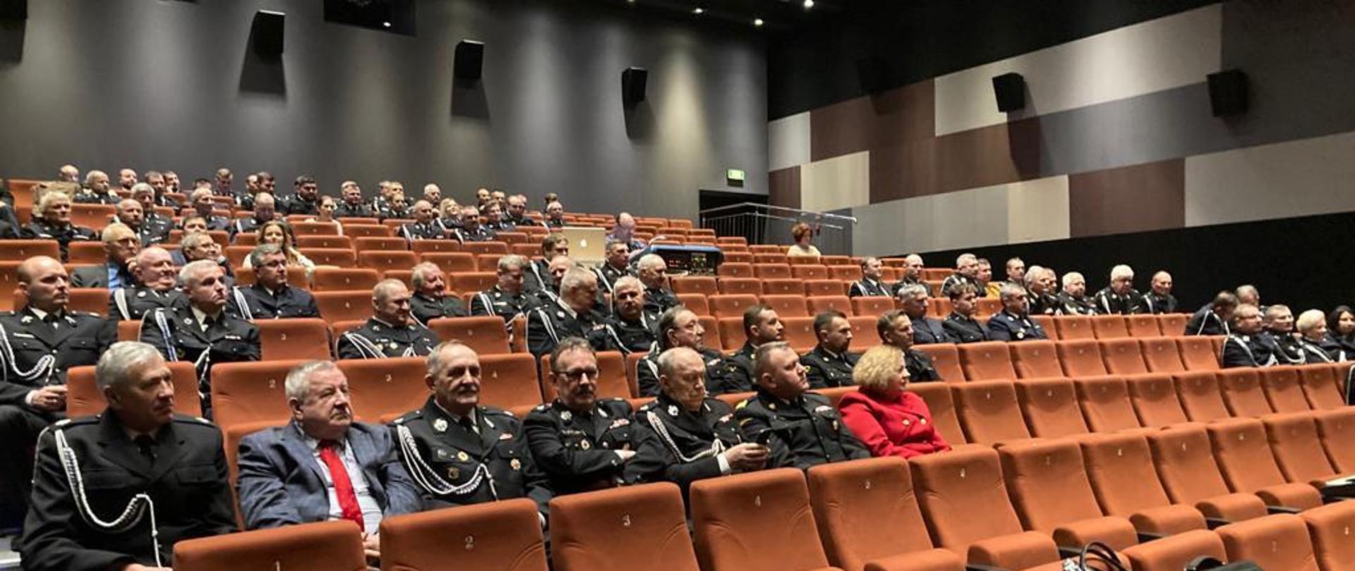 w sali widowiskowej siedzą strażacy oraz osoby cywilne