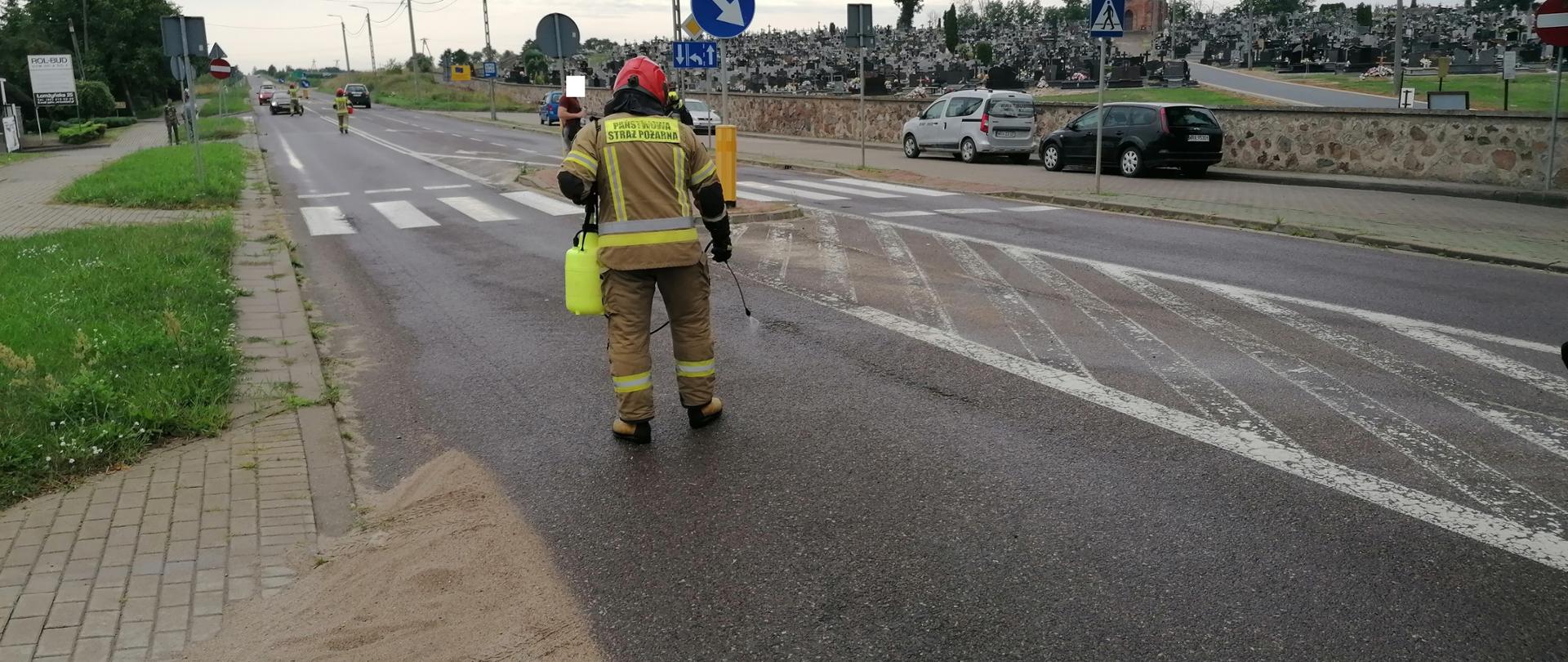 Strażak PSP prowadzi oprysk neutralizatorem do substancji ropopochodnych po jezdni.