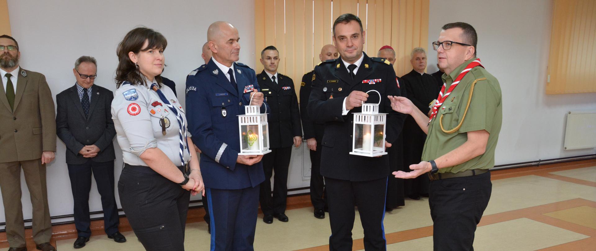 Na zdjęciu harcerze przekazują strażakowi i policjantowi światełko pokoju. 
