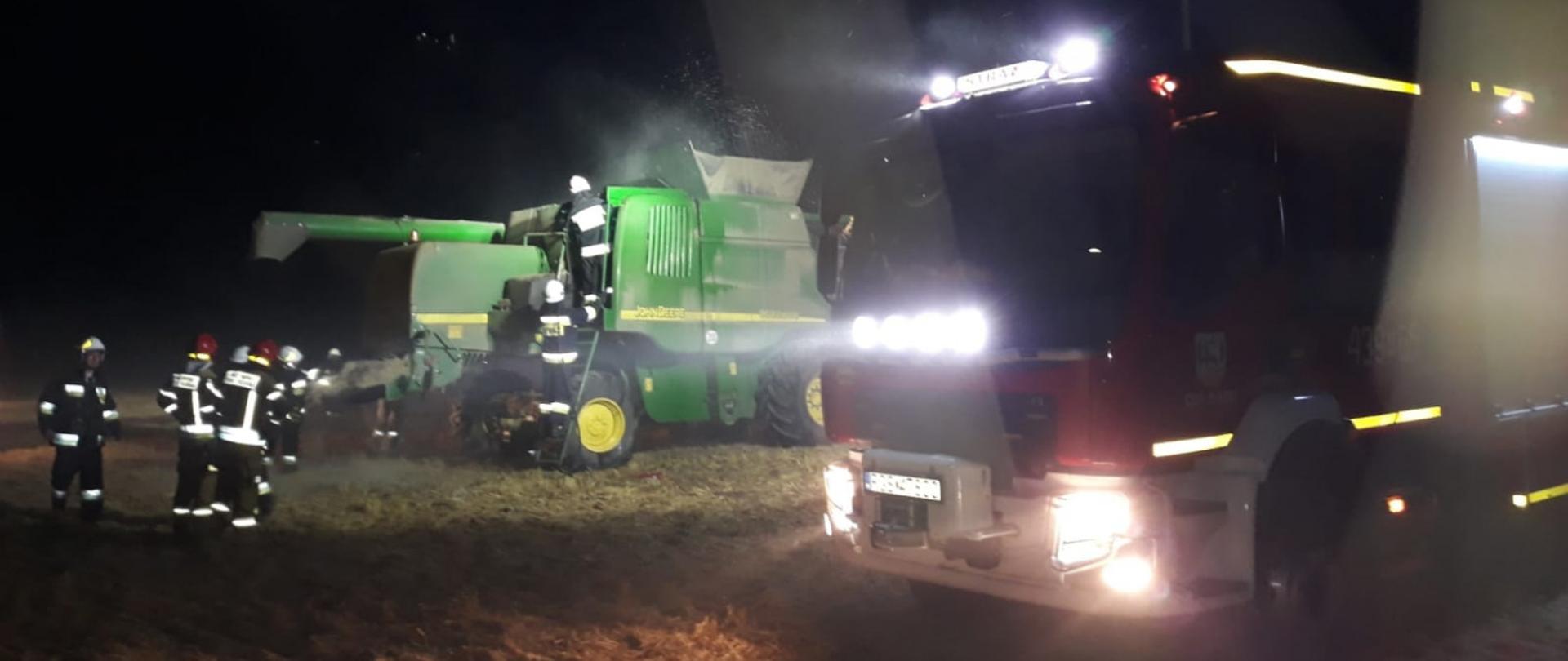 Zdjęcie przedstawia strażaków oraz kombajn i wóz strażacki stojące na polu.
