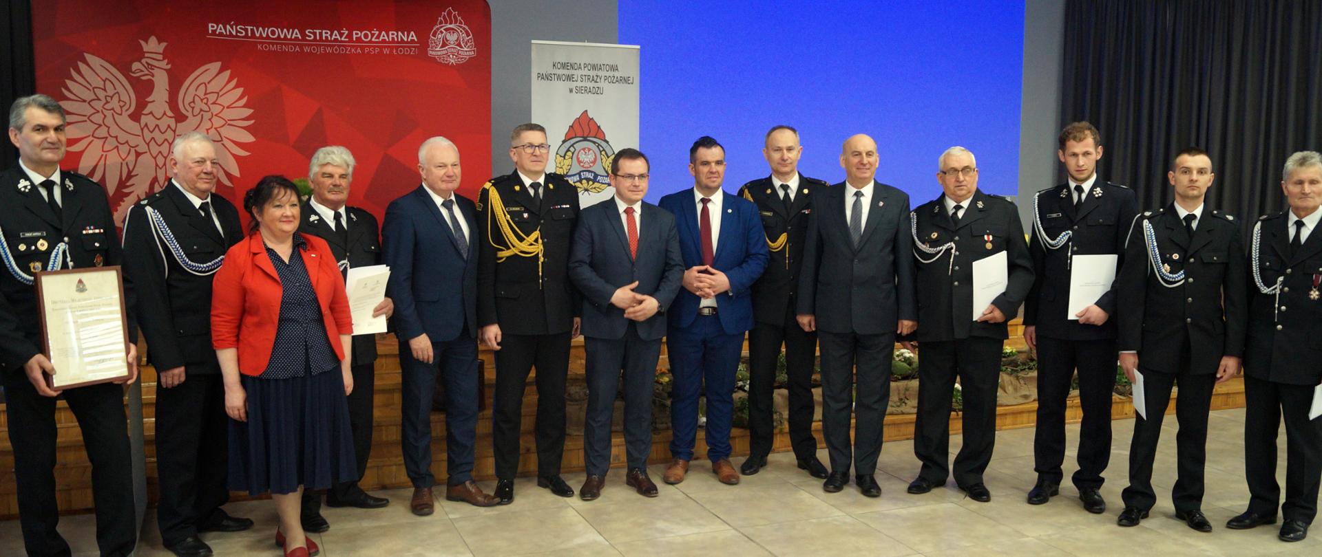 pamiątkowe zdjęcie druhów którzy otrzymali akty włączenia do ksrg, promesy na zakup samochodów oraz decyzje o przyznaniu świadczenia ratowniczego z nadbrygadierem Krzysztofem Hejdukiem Zastępcą Komendanta Głównego PSP oraz przedstawicielami Polskiego Parlamentu