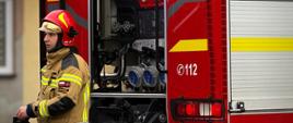 Na zdjęciu widoczny jest strażak na tle samochodu ratowniczo-gaśniczego.