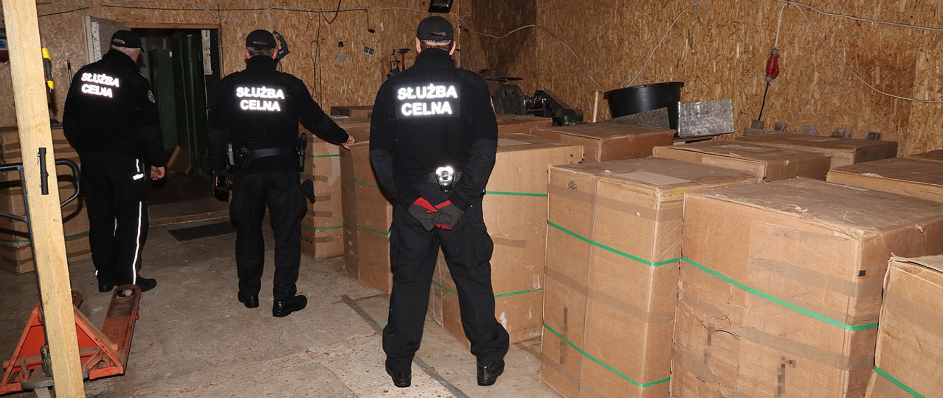 Trzech funkcjonariuszy wewnątrz pomieszczenia z kartonami.