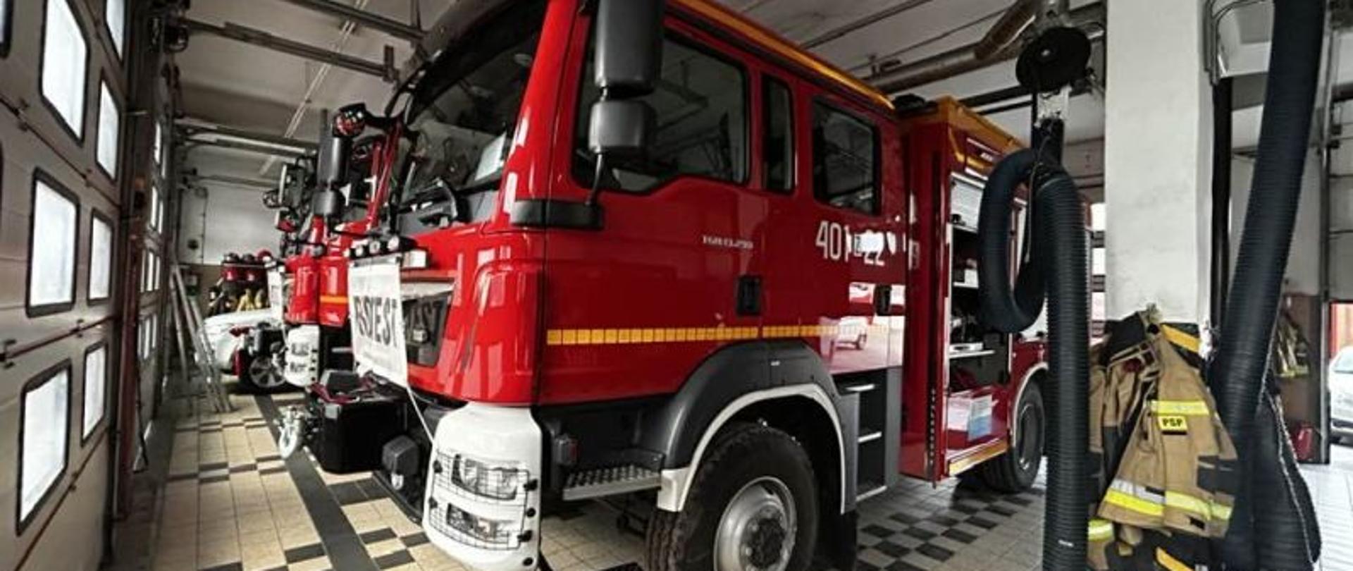 Widok na auto gaśnicze, koloru czerwonego. Widok na przód. Auto stoi na garażu.