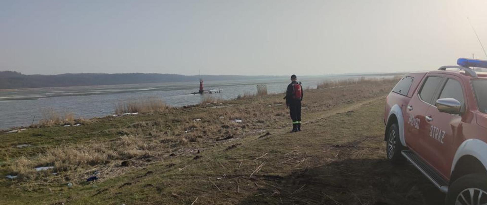 Na zdjęciu widać strażaka z samochodem operacyjnym kontrolującym poziom wody