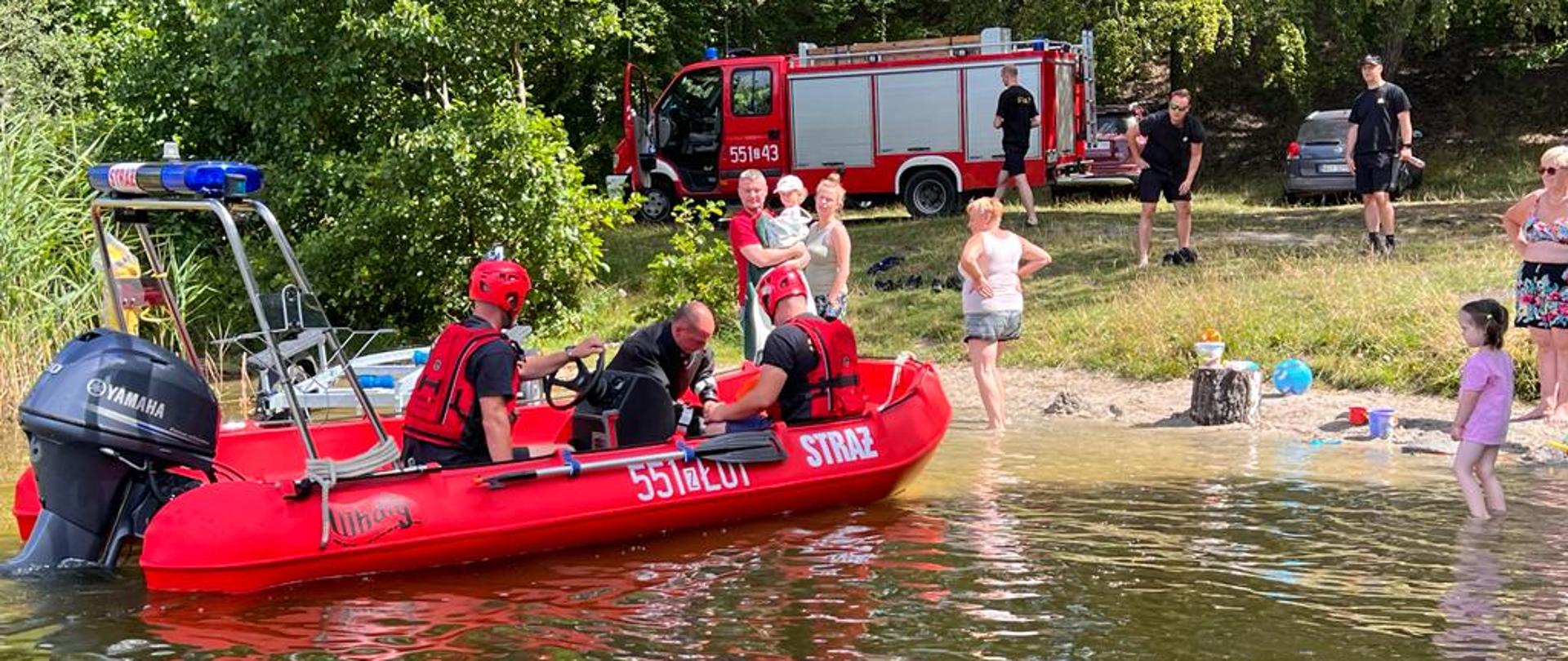 Zdjęcie przedstawia jezioro oraz czerwoną łódź ratowniczą na której ćwiczą strażacy.