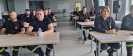 Strażacy osp siedzą i słuchają o zasadach przeprowadzenia egzaminu. 
