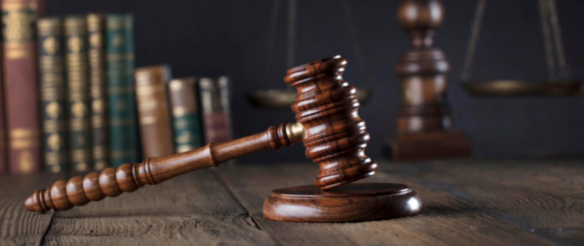 Blat biurka. Na nim młotek sędziowski na podstawce. W tle książki.