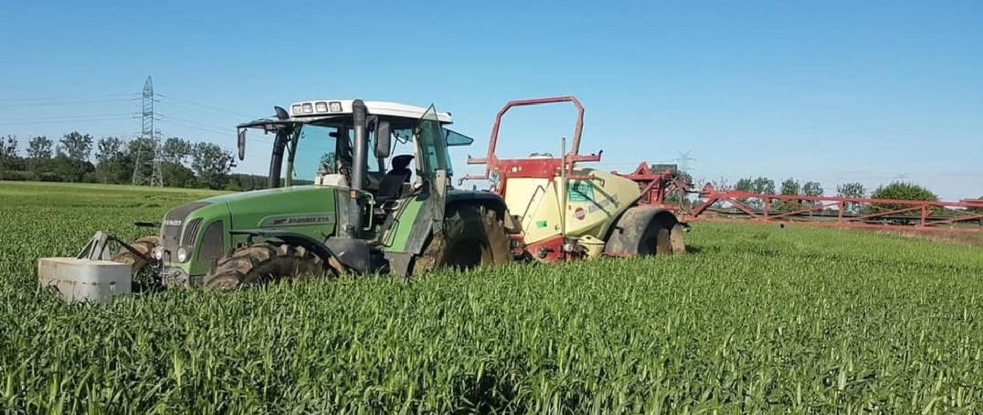 Zdjęcie przedstawia traktor z opryskiwaczem na polu