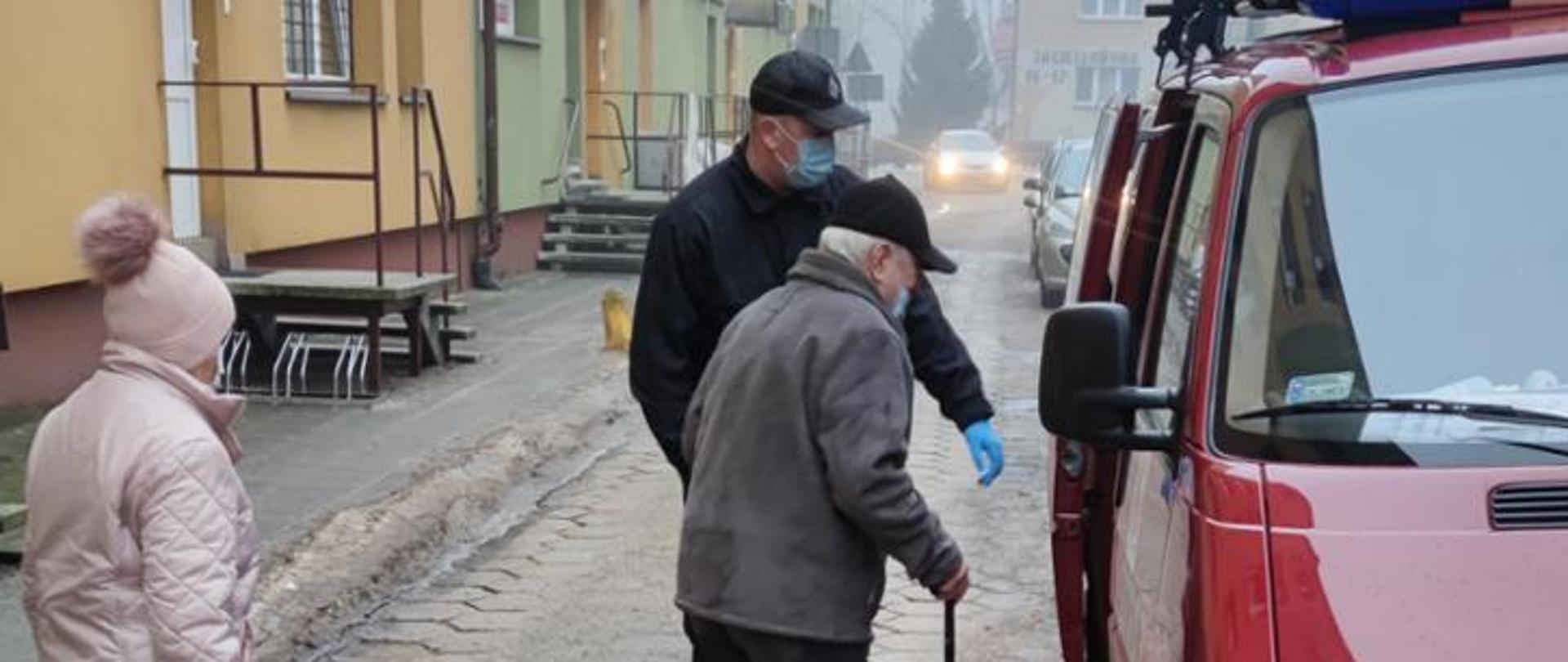 strażak pomaga w wejściu do samochodu strażackiego dwóm seniorom , pomoc w transporcie na szczepienie