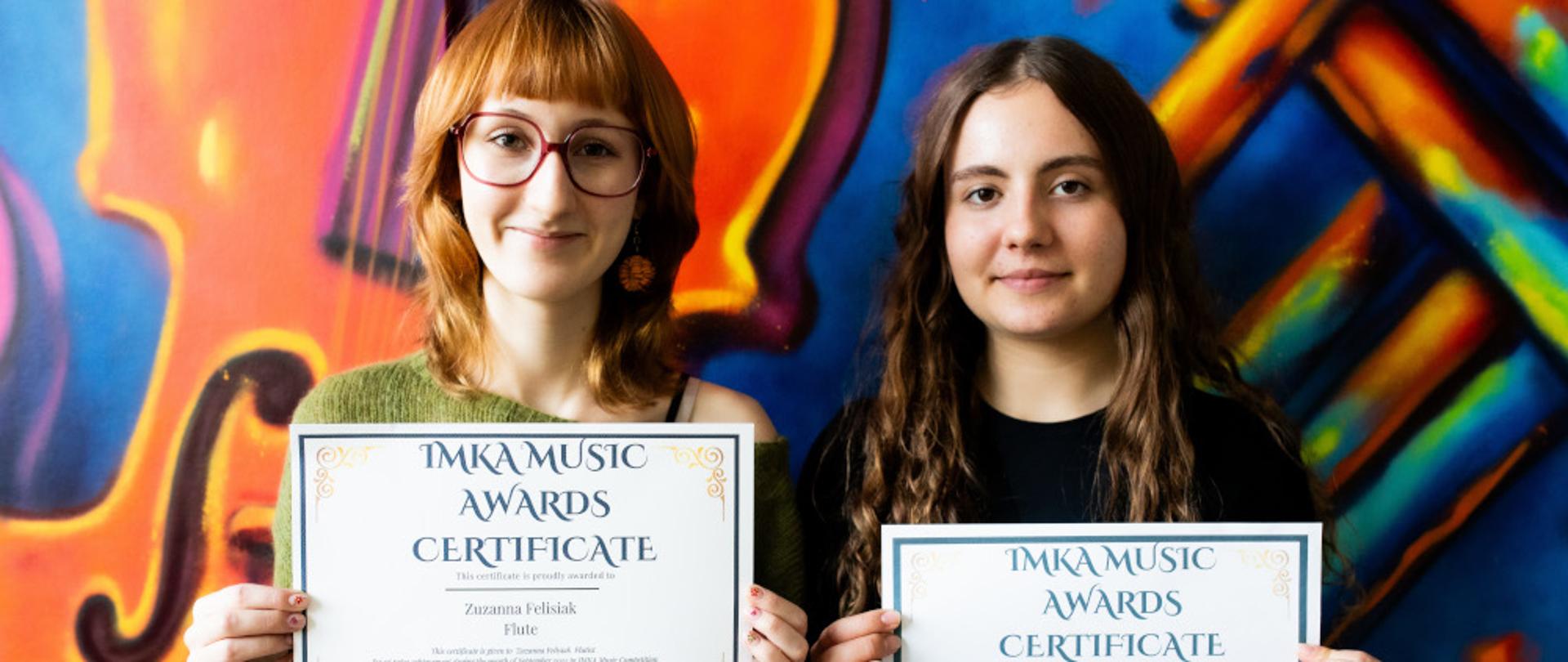 Uczennice ZPSM trzymają w rękach dyplomy, na tle kolorowej ściany