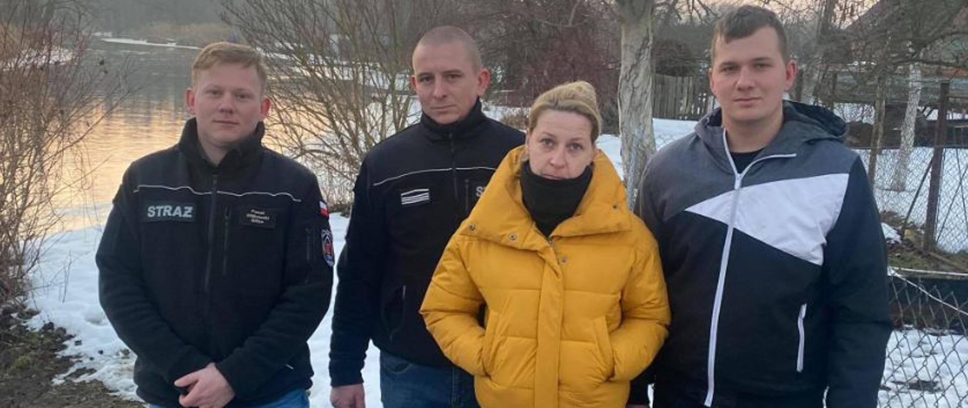 Na zdjęciu stoi od lewej Paweł Witkowski, Wojciech Szymański, ubrani w polary ze strażackimi emblematami, następnie kobieta w kurtce i pierwszy od prawej Mateusz Wyka ubrany w bluzę dresową. Za nimi w tle widać rzekę Wdę.
