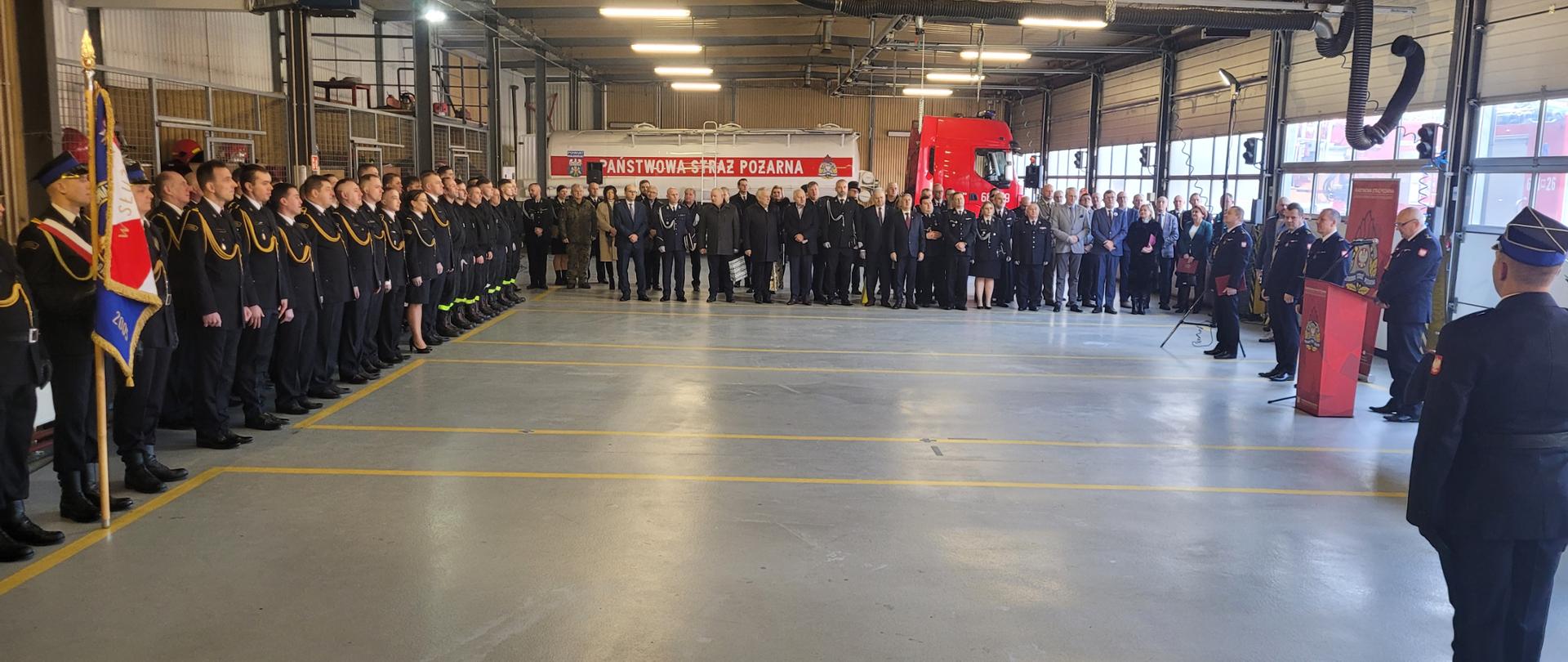 Zdjęcia przedstawiają uroczystość zdania i objęcia pełnienia obowiązków Komendanta Powiatowego PSP w Wołominie. Na zdjęciach widoczni są strażacy w umundurowaniu wyjściowym oraz zaproszeni goście. Uroczystość odbywa się na garażu JRG.